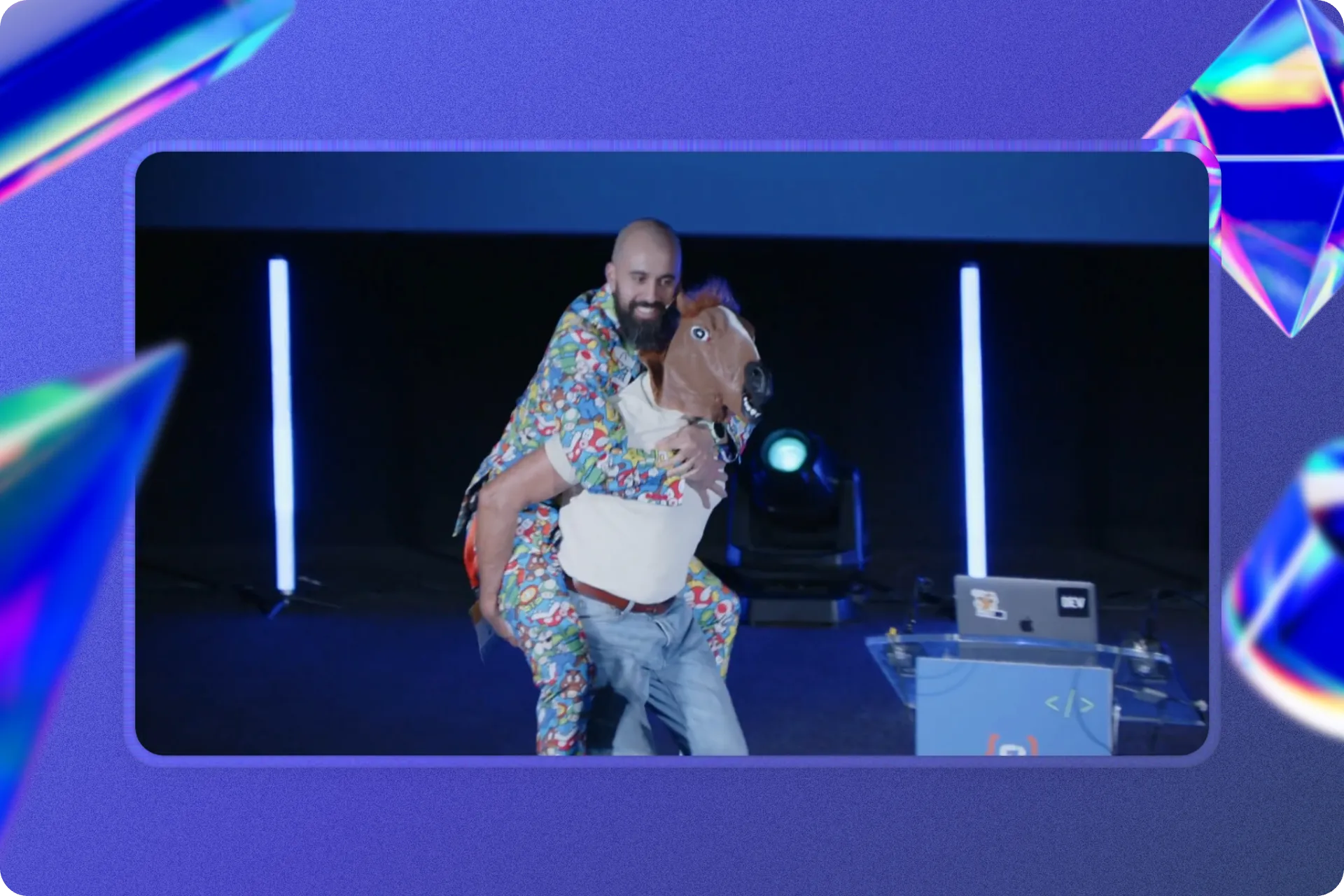 En un escenario de conferencia, aparece Jorge Baumann con un traje colorido estampado de Super Mario sonriendo mientras va a caballito sobre otra persona (su padre) que lleva una máscara de caballo. Detrás se ven luces verticales azules y un atril con un portátil con pegatinas.